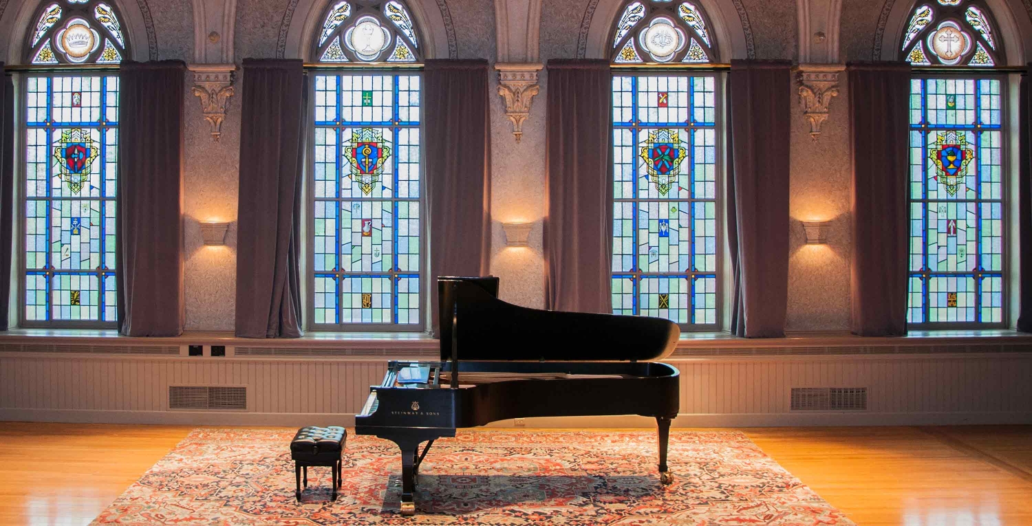 a fine arts space at college of the holy cross features a piano in front of stained glass windows