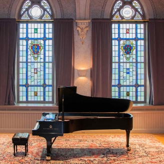 a fine arts space at college of the holy cross features a piano in front of stained glass windows
