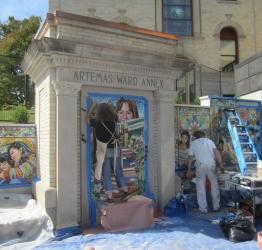 an artist paints a mural on a recovered historic entrance