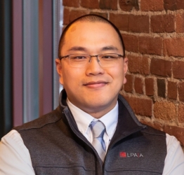 Chris Lee stands in front of a window and brick wall in the office