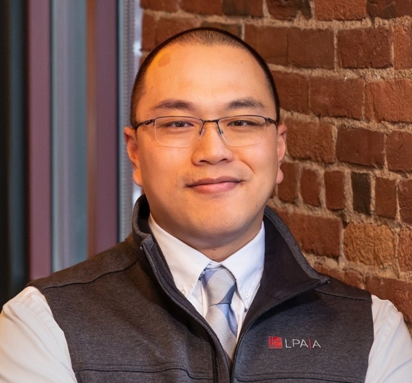 Chris Lee stands in front of a window and brick wall in the office