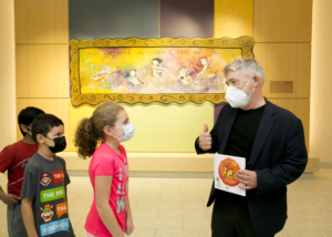 Peter Reynolds in the hallway of the Beal Elementary School talking to young students in front of a mural he had painted