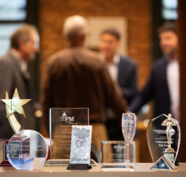 several awards in the foreground while several people are gathered in the background engaged in conversation